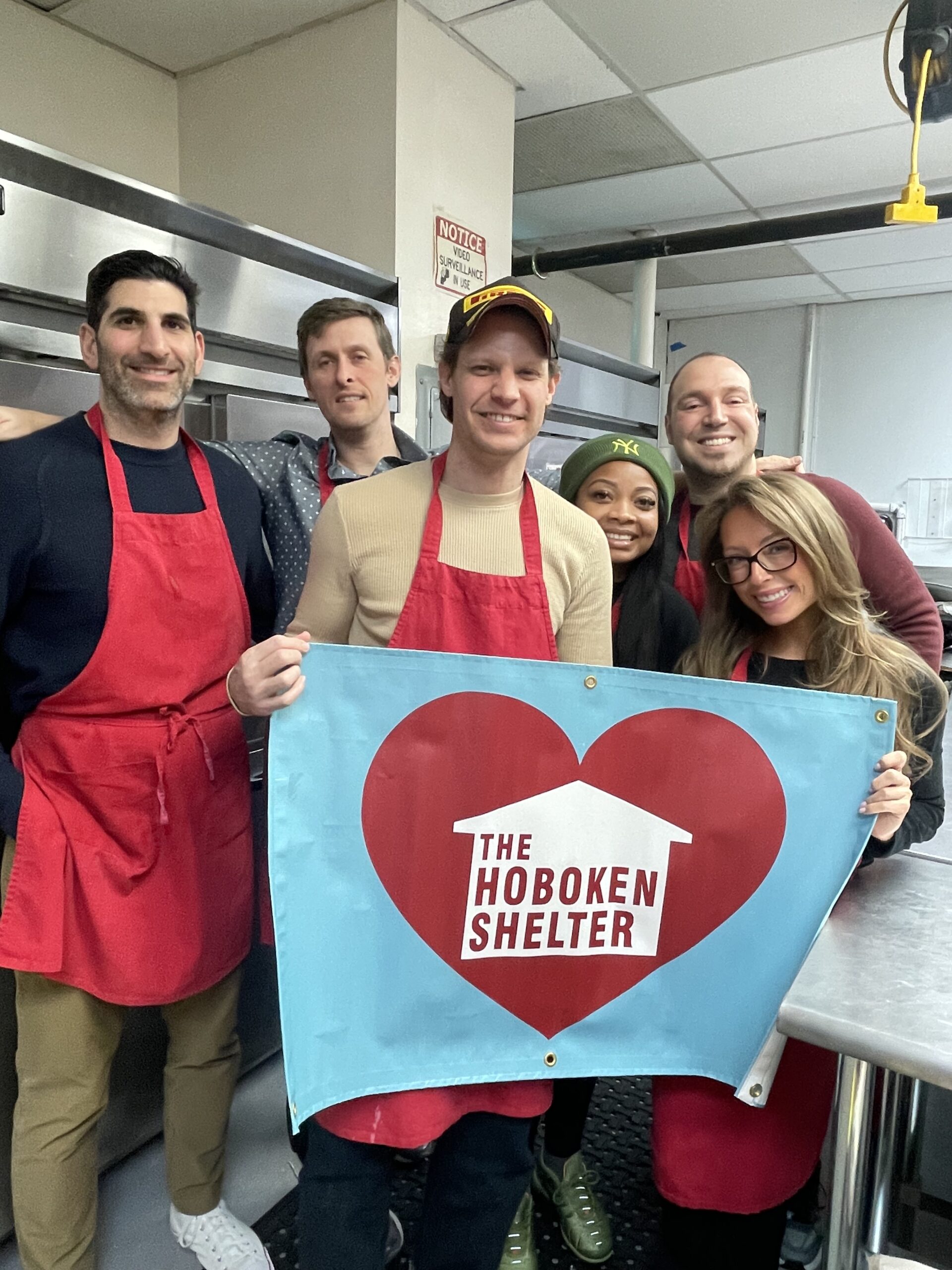 Tire Agent A group of men and women from Tire Agent holding the Hoboken Shelter banner heart logo sign.